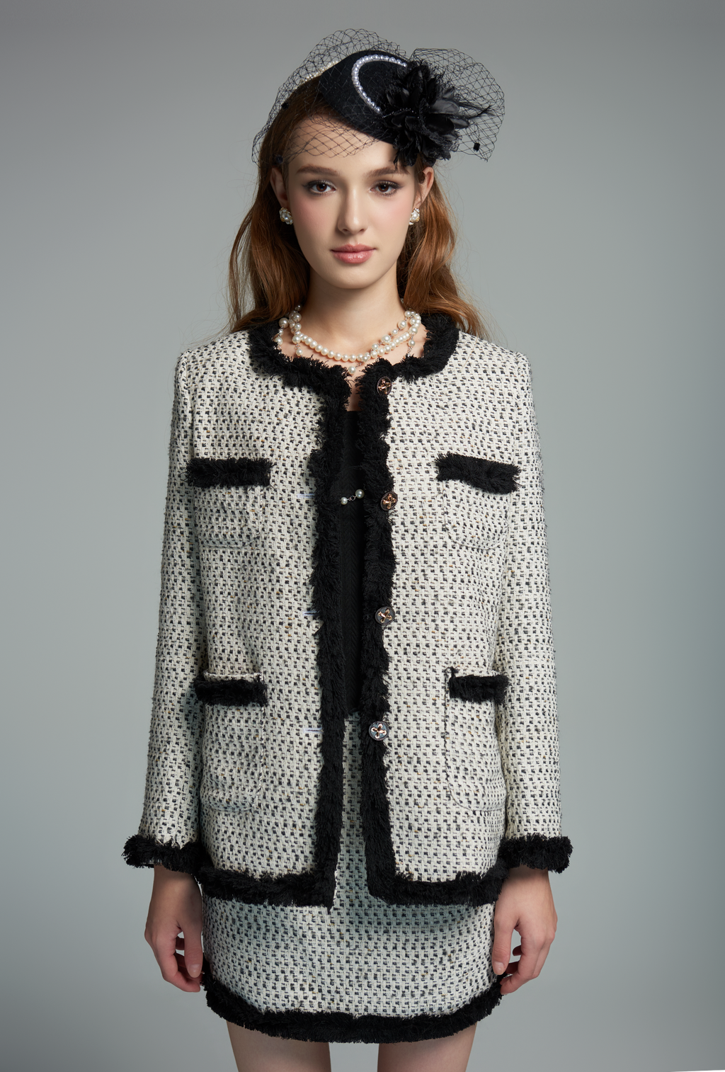 Woman wearing a black and white textured suit with a matching hat on a gray background